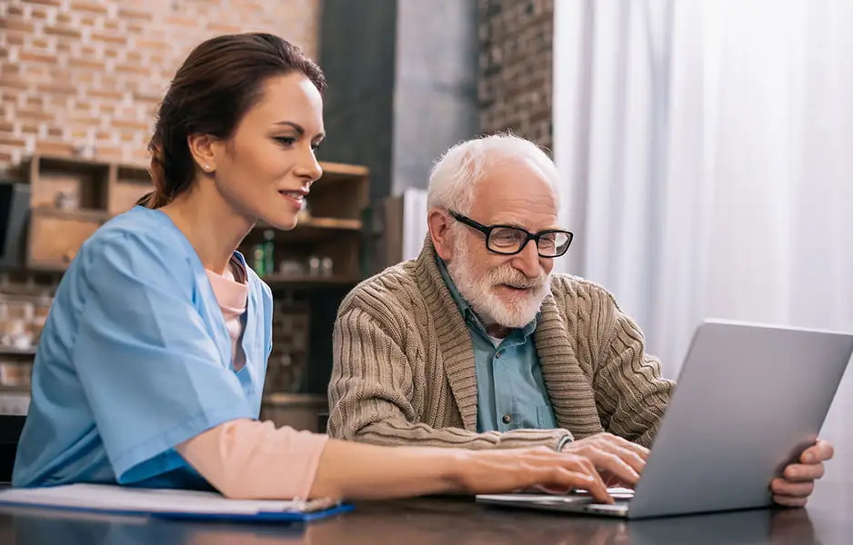 a young female nurse helping an elderly man with his laptop